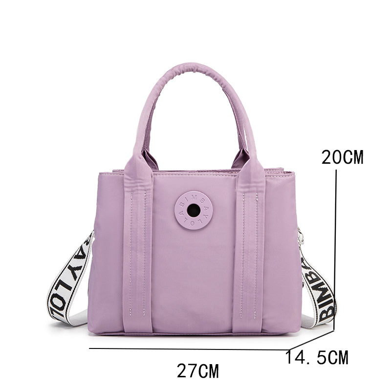 A stylish and structured mini tote designed for everyday elegance. Crafted from durable lightweight nylon in a soft lavender tone, it features dual top handles and a bold adjustable logo strap for versatile carry options