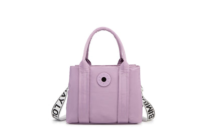 A stylish and structured mini tote designed for everyday elegance. Crafted from durable lightweight nylon in a soft lavender tone, it features dual top handles and a bold adjustable logo strap for versatile carry options